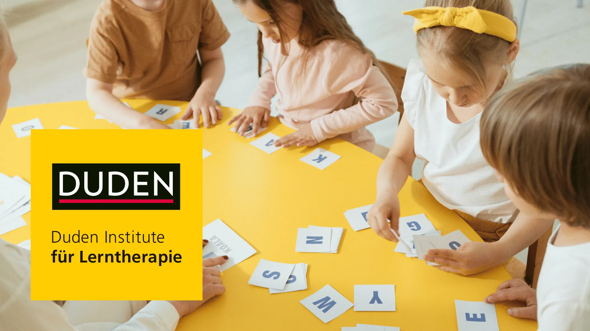Kinder spielen an einem Tisch mit Buchstabenkarten 