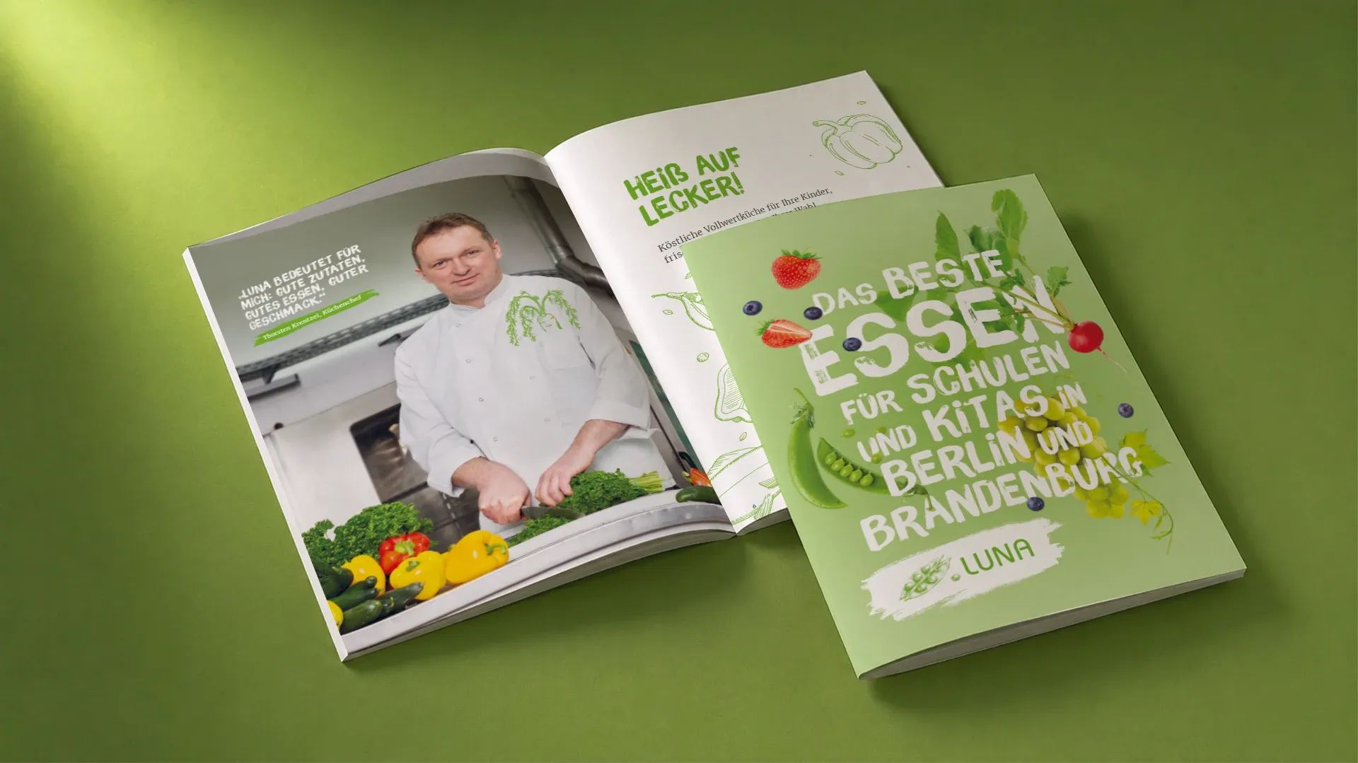Aufgeschlagene LUNA-Broschüre mit dem Cover-Titel „Das beste Essen für Schulen und Kitas in Berlin und Brandenburg" und einer Innenseite mit einem Koch beim Gemüseschneiden.