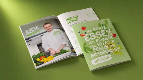Aufgeschlagene LUNA-Broschüre mit dem Cover-Titel „Das beste Essen für Schulen und Kitas in Berlin und Brandenburg" und einer Innenseite mit einem Koch beim Gemüseschneiden.